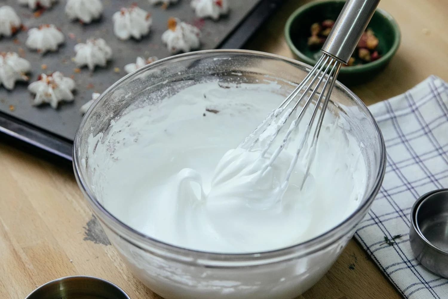 Ciotola di albumi montati a neve accanto a tuorlo separato e piccole meringhe