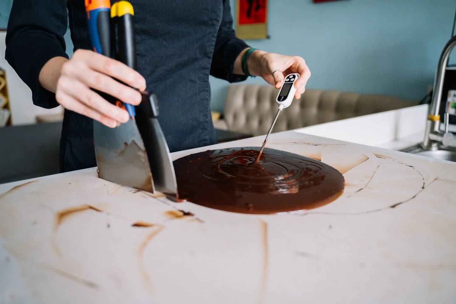 Mani al lavoro con due spatole e un termometro nel cioccolato fuso su un piano di marmo