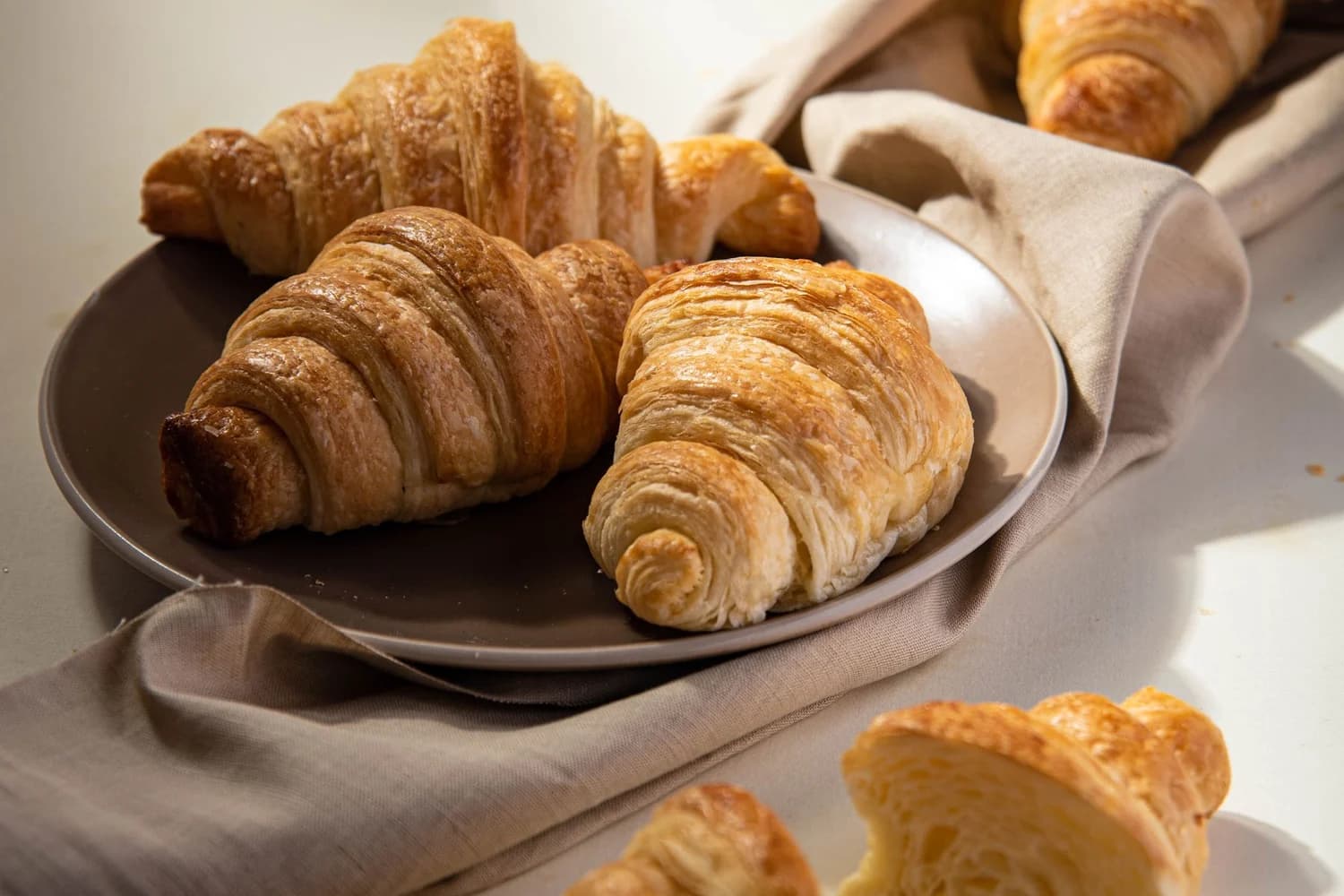 Cornetti dorati e sfogliati su un piatto, con un cornetto tagliato in primo piano
