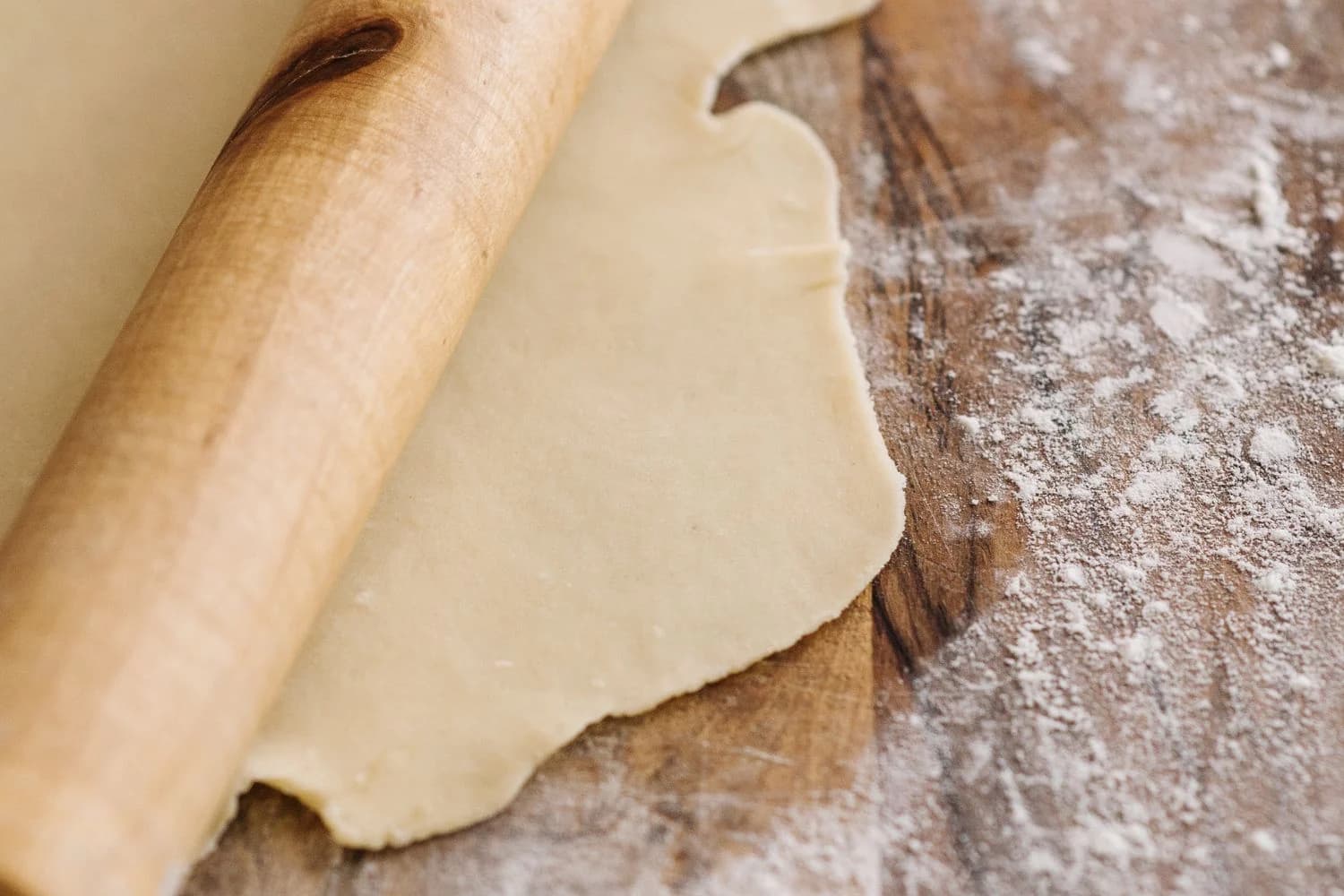 Mattarello in legno su un impasto steso, con farina sul piano di lavoro