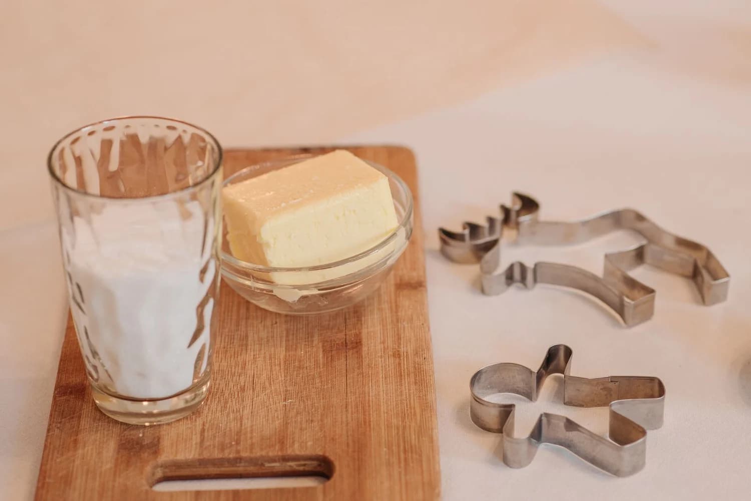 Bicchiere di latte e panetto di burro sul tagliere, accanto agli stampini per biscotti